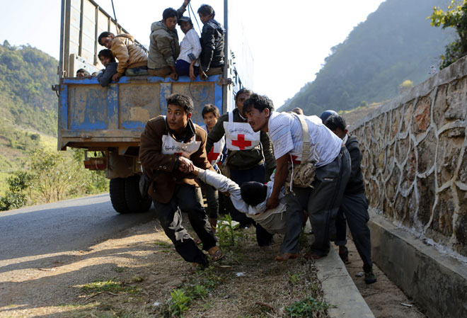 Volunteers of Myanmar Red Cross organisation carry wounded volunteer U Moe Kyaw, 45, as the war vrefugees fleeing from Laukkai sit on the truck after vehicles of a rescue convoy were attacked by Kokang rebels near Kokang capital Laukkai, northern Shan State, Myanmar, February 17, 2015. Two volunteers from Myanmar Red Cross Society injured in rescue convoy attack. Photo: Lynn Bo Bo/EPA