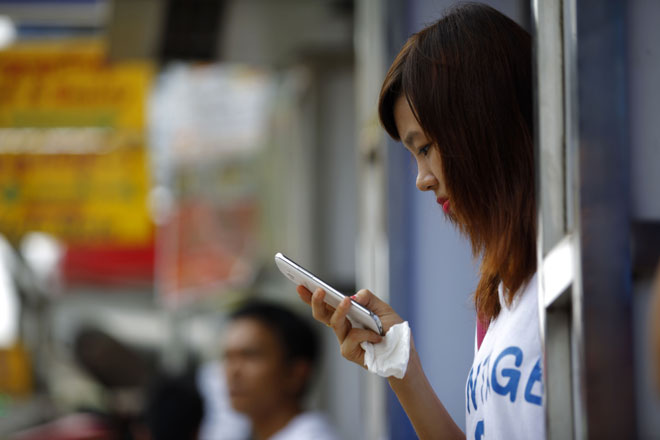 A girl using her mobile phone on the roadside in Yangon, Myanmar, April 4, 2014.Photo: Lynn Bo Bo/EPA