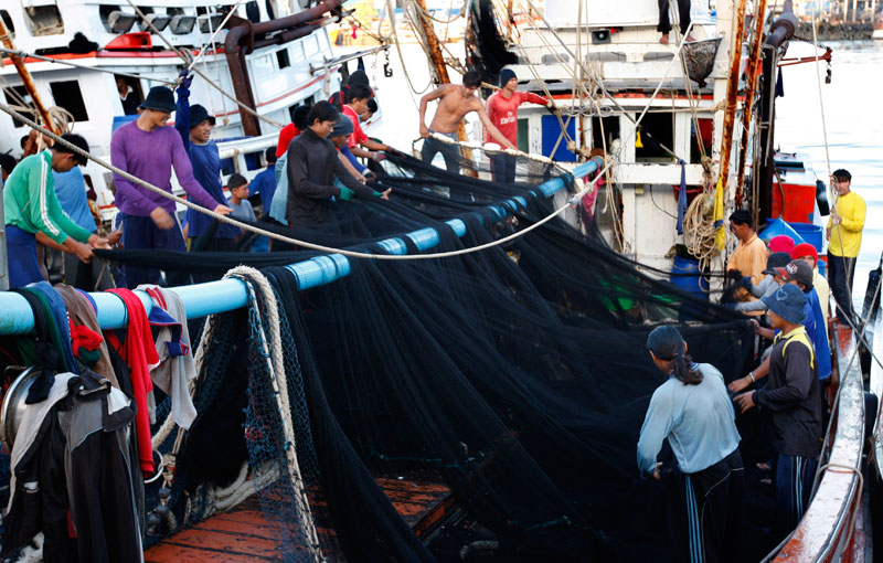 Myanmar migrant workers check and fold the fishing nets after they unload the catch at the fishing port on Si Rae island, off Phuket, southern Thailand. Photo: Barbara Walton/EPA