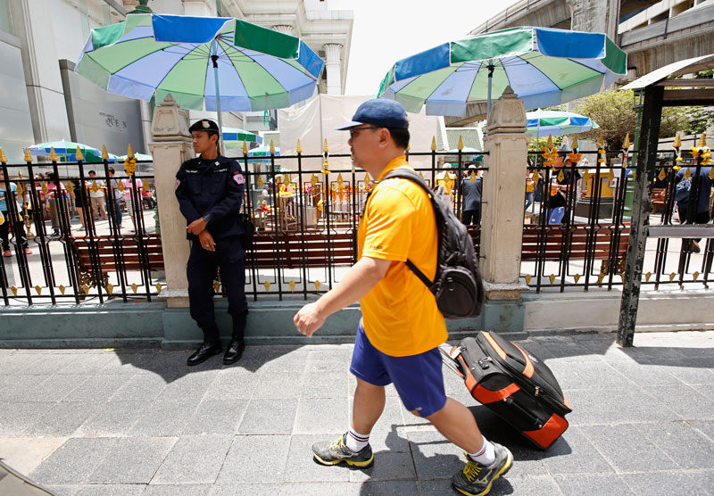 A Thai police officer on duty as a tourist with luggage walks past the Erawan Shrine in Bangkok, Thailand, 30 August 2015. Photo: Rungroj Yongrit/EPA