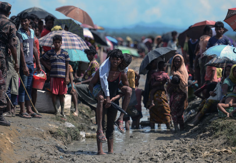 (FILES) In this file photo taken on October 17, 2017 a Rohingya refugee carries an old man in an area near no man's land on the Bangladesh side of the border with Myanmar after crossing the Naf River, after being told by border guards they were not allowed to leave the area and reach the refugee camps near Ukhia. Photo: Munir Uz Zaman/AFP
