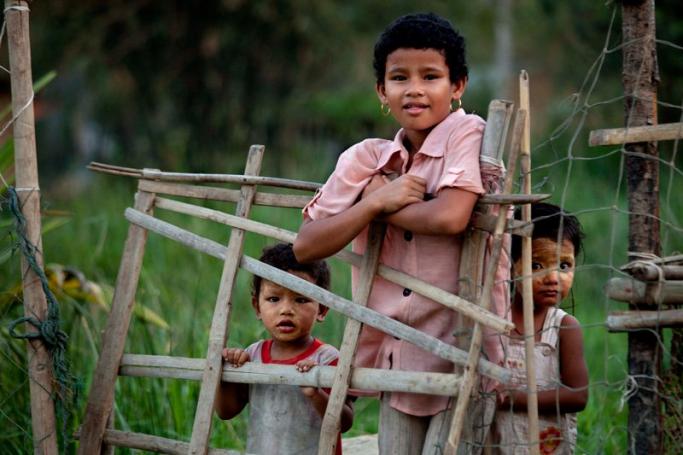 Children stand behind the fence of a house near a dockyard in Dala, on the outskirts of Yangon City, Myanmar. Photo: Lynn Bo Bo/EPA