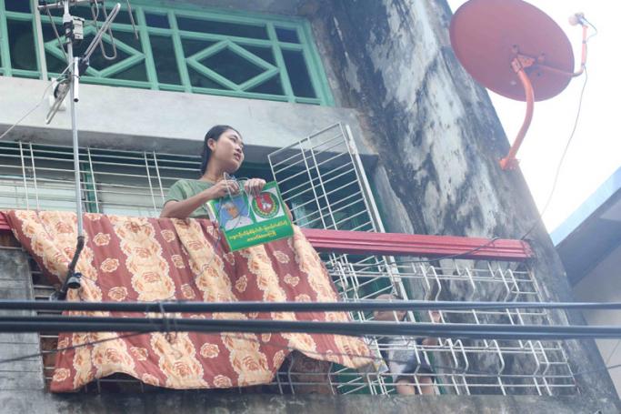 A woman on a balcony in an apartment block in Thinganggyun Township, Yangon, with USDP campaign material bearing the president's image, on Nov. 3. (PHOTO: Myanmar Now/Phyo Thiha Cho)