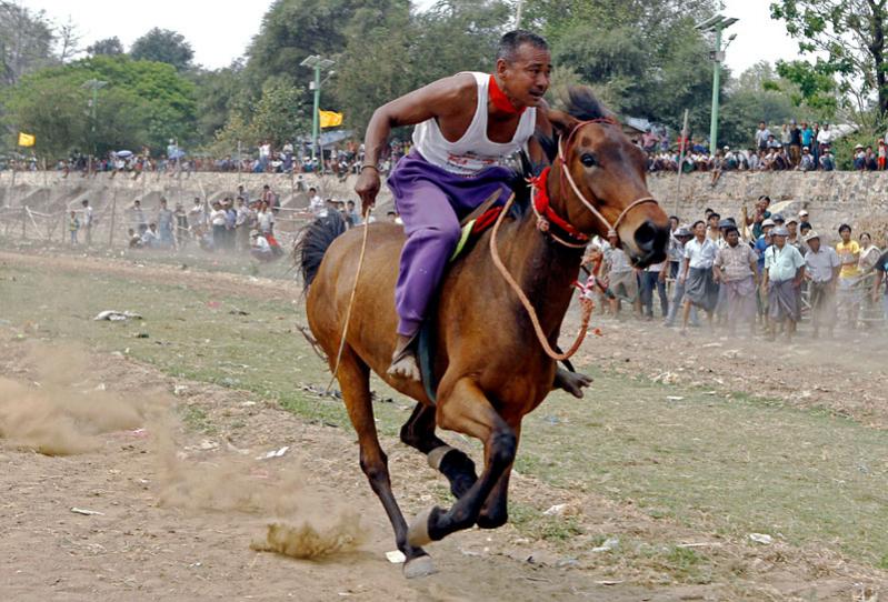 A jockey rides during the horse racing at a pagoda festival at Taungthaman Lake near U Pain Bridge in Amarapura, Mandalay, Myanmar, March 24, 2015. Photo: Pyae Sone Aung/EPA