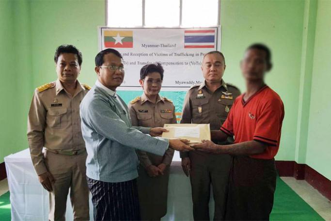 An official hands over compensation to a victim trafficked to Thailand. Photo: Myanmar News Agency
