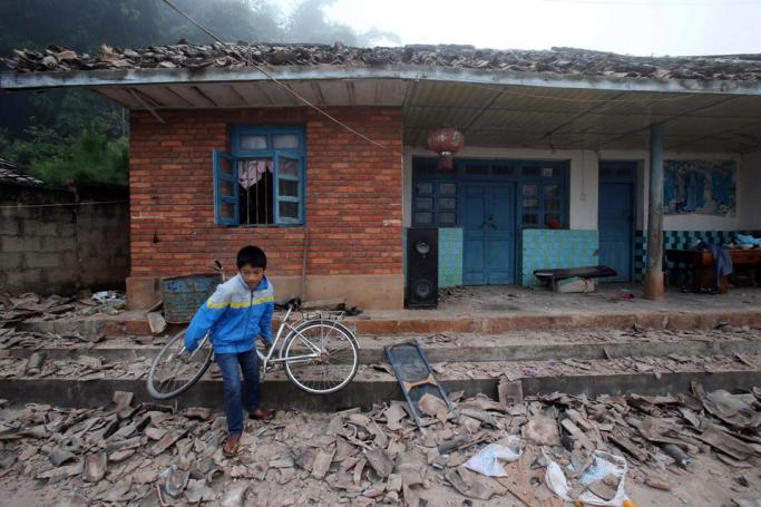 A boy lifts a bike amid debris outside a damaged house in Jinggu county, Yunnan province, China, 08 October 2014. A 6.6-magnitude earthquake jolted Jinggu on 07 October night, killing at least one person and injuring 324 so far. Photo: EPA
