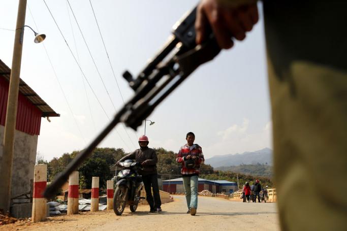 People walk past as armed soldier takes guards at the entrance of Chin Shwe Haw town of Kokang self-administered area, northern Shan State, Myanmar, 16 February 2015. Photo: Lynn Bo Bo/EPA
