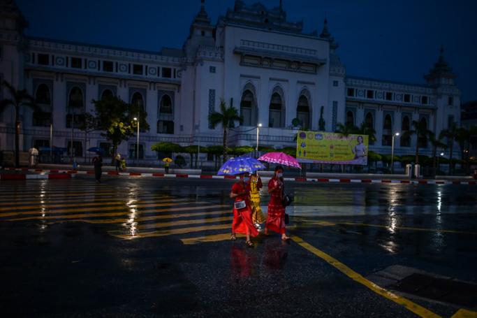 People holding umbrellas as they cross the road during rainfall in Yangon. Photo: Ye Aung Thu/AFP