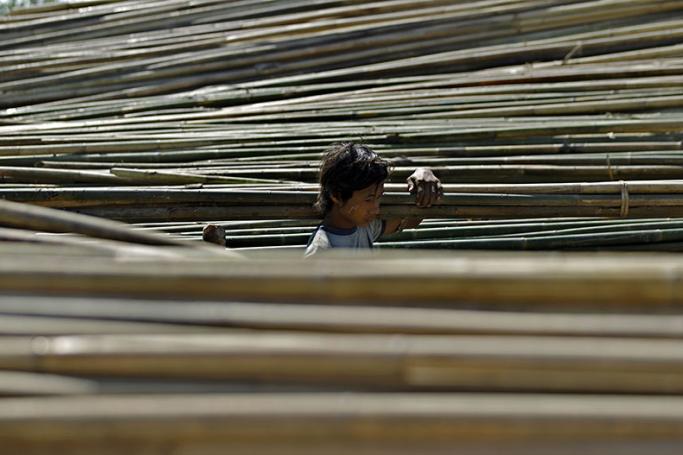 A man loads bamboo poles on his shoulder as he walks passed piles of bamboo poles. Photo: Lynn Bo Bo/EPA
