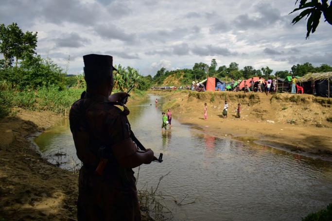 (File) This August 29, 2017 photo taken from Nykkhongchhari near the Bangladeshi town of Ukhiya shows a Bangladeshi border guard ordering Rohingya refugees to return to the Myanmar side of a small canal between the two countries. Photo: Emrul Kamal/AFP

