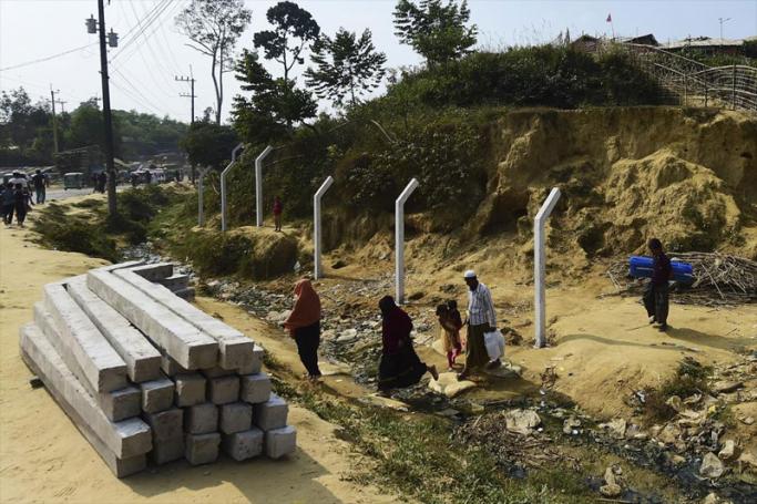 Rohingya refugees walk past a pile of concrete pillars as authorities prepare erecting pillars for barbed-wire fences around Balukhali refugee camp in Ukhia on December 10. (Photo: AFP)