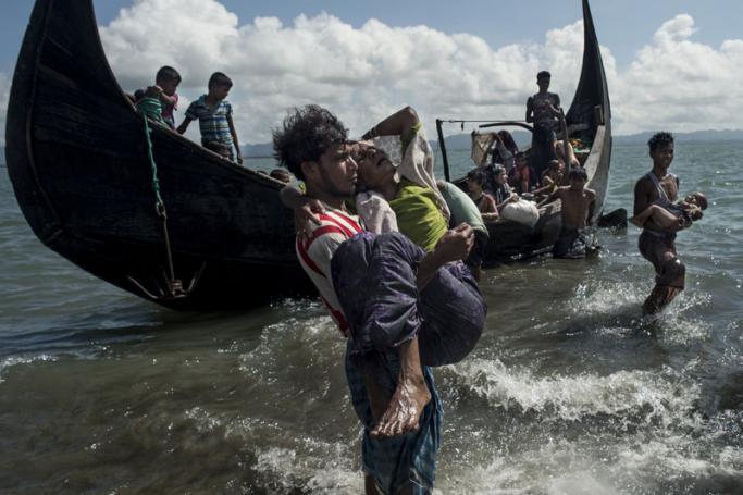 A Bangladeshi man helps Rohingya Muslim refugees to disembark from a boat on the Bangladeshi shoreline of the Naf river after crossing the border from Myanmar in Teknaf on September 30, 2017. Photo: Fred Dufour/AFP
