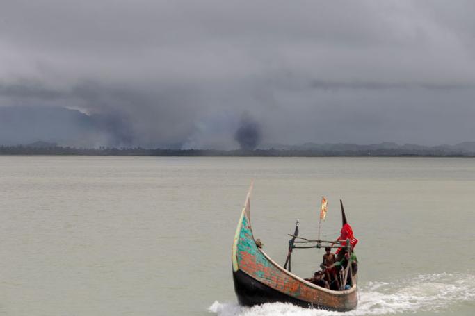 This photograph taken on September 12, 2017 shows Rohingya refugees arriving by boat, as smoke rises from fires on the shoreline behind them, at Shah Parir Dwip on the Bangladesh side of the Naf River after fleeing violence in Myanmar. Photo: Adib Chowdhury/AFP
