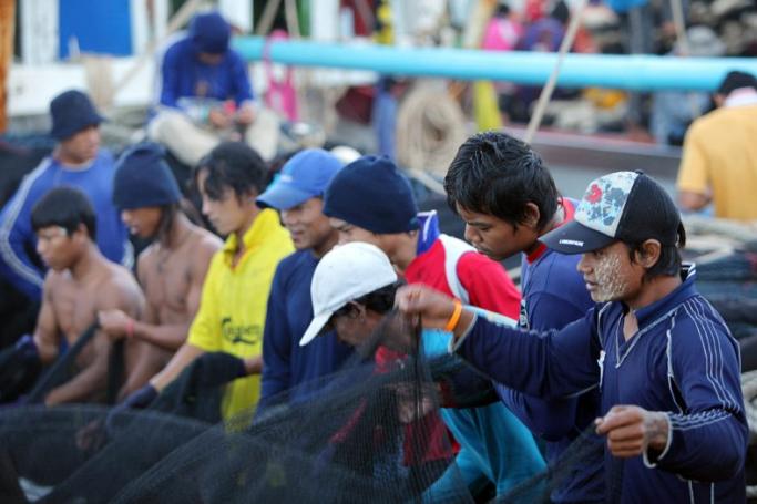 Myanmar migrant workers check and fold the fishing nets after they  unload the catch at the fishing port on Si Rae island, off Phuket, southern Thailand. Photo: Barbara Walton/EPA
