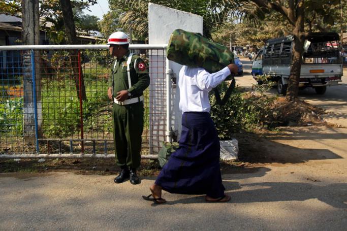 (File) Myanmar boy wearing a white shirt (R), who was discharged from Myanmar army, loads a bag on his shoulder as he walks near a military man at a gate of military compound  - 18 January 2014. Photo: Lynn Bo Bo/EPA