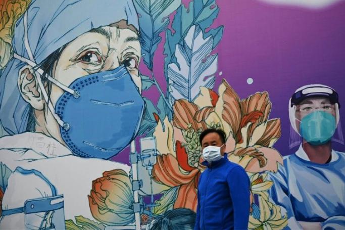 A man wearing a facemask walks in front of a mural at Leishenshan Hospital in Wuhan, China (AFP Photo/Noel Celis) 