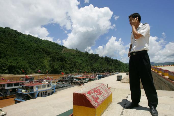A Chinese border inspection guard talks on his cell phone while looking across to Myanmar (green hills) and boats docked along the Mekong River (or Lancang River within China) in Guanlei, in Xishuangbanna Dai Autonomous Prefecture which borders Myanmar and Laos in China's southwest Yunnan province. Photo: AFP
