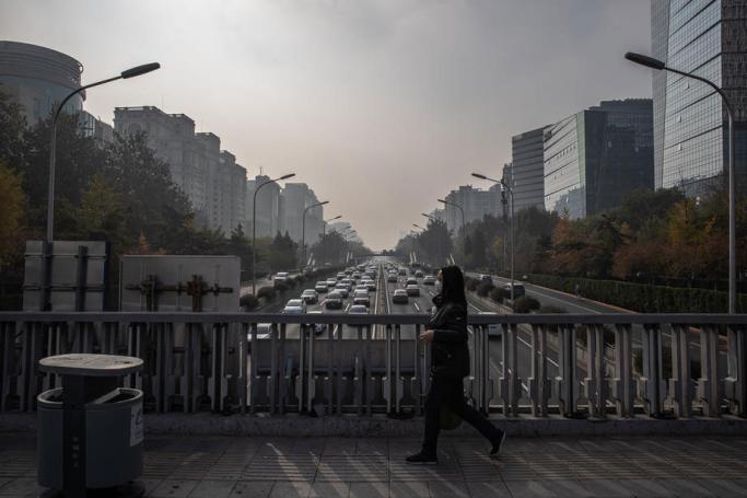 A woman walks on a bridge over a road carrying cars on a polluted day in Beijing, China. Photo: EPA