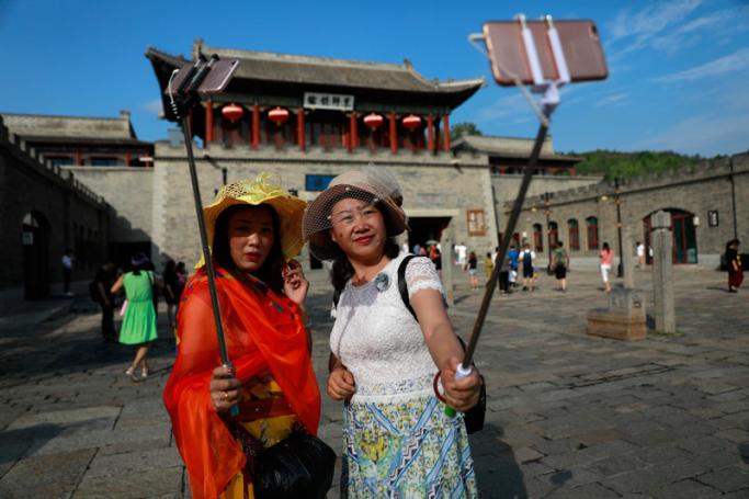 Chinese visitors take selfies with their mobile phones on selfie sticks at the entrance of Gubeishui town at the bottom of the Simatai Great Wall in Miyun county, 120 kilometers northeast of Beijing, China, 23 July 2017. Photo: How Hwee Young/EPA

