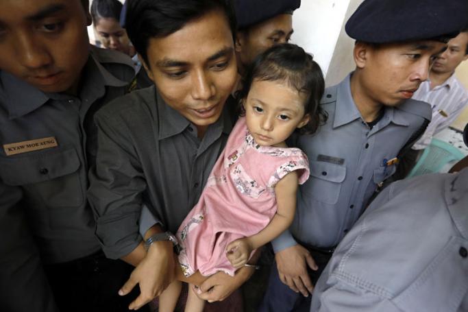Detained Reuters journalist Kyaw Soe Oo (C) holds his daughter, as he is escorted by police as he arrives to court in Yangon, Myanmar, 21 March 2018. Photo: Nyein Chan Naing/EPA-EFE
