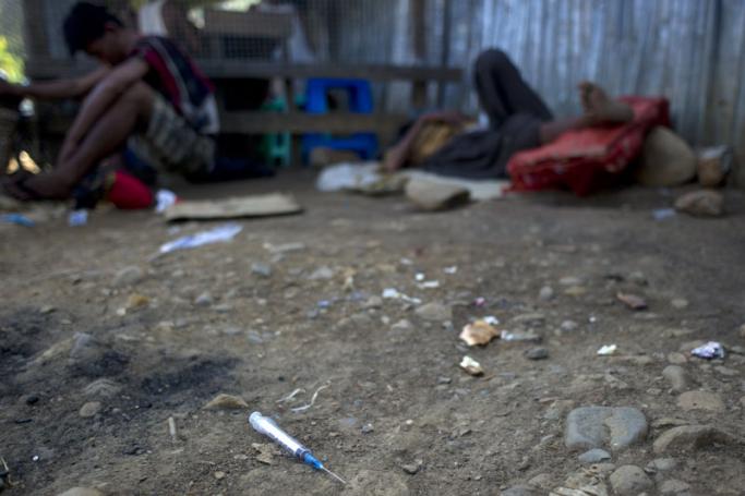 A freshly discarded hypodermic syringe lies near drug users (back) who slept in a village near a jade mine in the township of Hpakant in Kachin State. Photo: Ye Aung Thu/AF