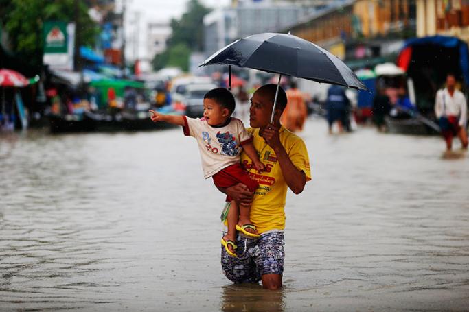 A man carries a chid as he walks along a flooded road in front of a shopping mall in Pathein City, capital of Ayeyarwady Region, Myanmar, 13 August 2016. Photo: Lynn Bo Bo/EPA
