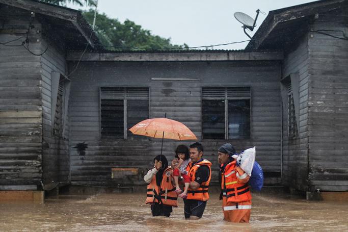 A Malaysia Civil Defence Force (JPAM) officer (R) accompanies a family as they wade through the flood during rain at Machang, Kelantan, around 400km from Kuala Lumpur, Malaysia, 3 January 2016. Photo: Ahmad Yusufi/EPA
