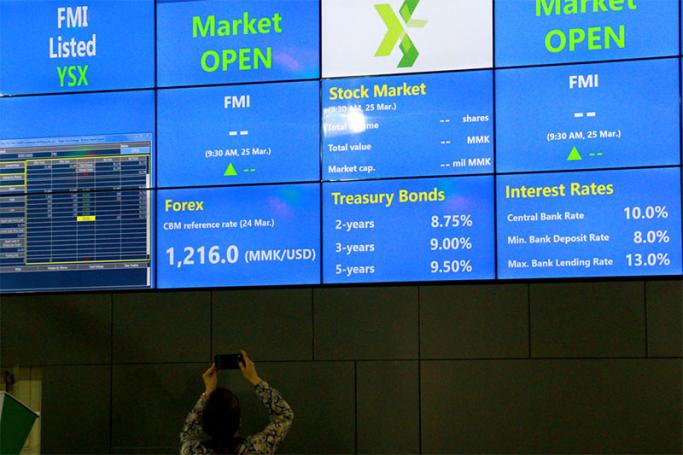 A woman takes a photograph of an electronic board showing the FMI (First Myanmar Investment) index at Yangon Stock Exchange, Yangon on 25 March 2016. Photo: Mizzima
