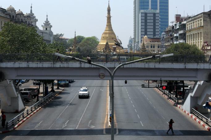 A woman crosses a nearly empty street near Sule Pagoda in Yangon as authorities handle cases of COVID-19 coronavirus on March 29, 2020. Photo: Sai Aung Main / AFP 