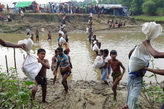 Refugees carrying aid across a river on the border with Bangladesh. Photo: ICRC
