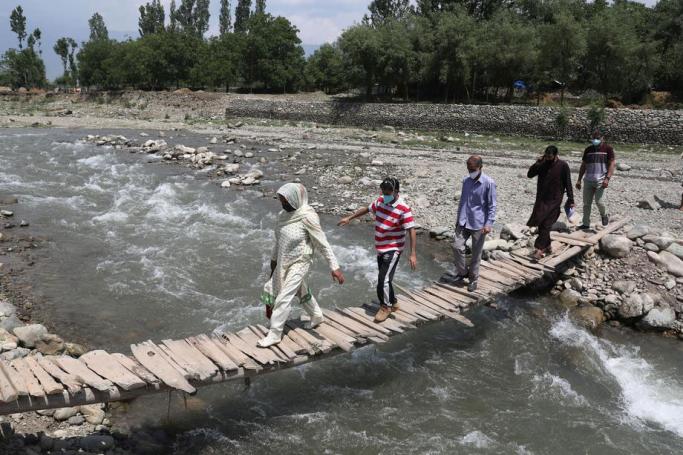 A doctor and health workers cross a wooden bridge during a Covid-19 vaccination drive in a village in Tral, some 35 km south of Srinagar, the summer capital of Indian Kashmir, 05 June 2021. Photo: EPA