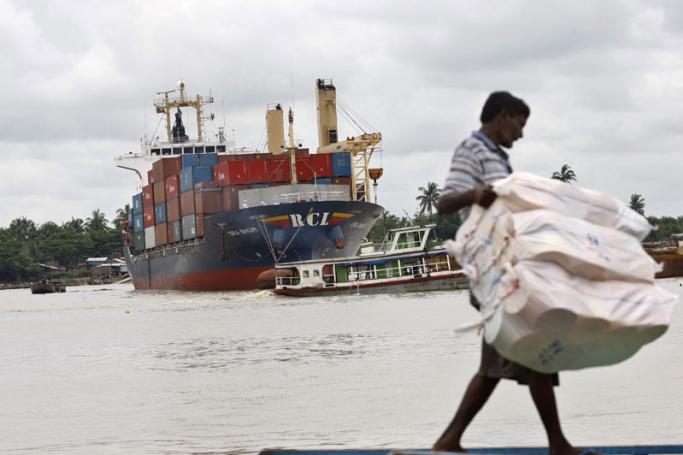 A Myanmar man carries goods at Yangon jetty as a cargo ship loads containers in the background on the Yangon river, Yangon. Photo: Lynn Bo Bo/EPA