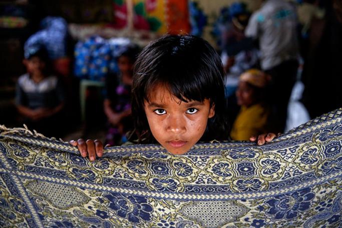 A Muslim Rohingya girl, stands behind a cloth to create a wall as her family gathers behind, while inside a shelter at the Thet Kel Pyin internally displaced person (IDP) camp in Rakhine State, near the capital of Sittwe, Myanmar, 10 March 2017. Photo: Lynn Bo Bo/EPA
