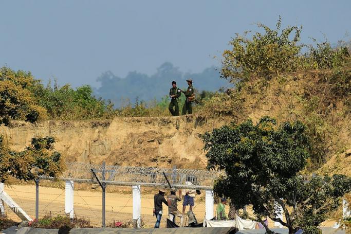 This photo taken on February 27, 2018 shows Myanmar army personnel keeping watch as Myanmar workers build a fence along the Myanmar-Bangladesh border, as seen from Tombru in the Bangladeshi district of Bandarban. Photo: Munir Uz Zam/AFP
