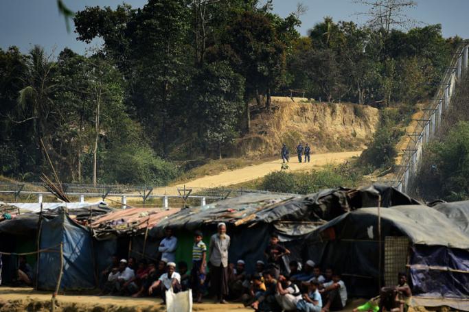 Myanmar security personnel keep watch along the Myanmar-Bangladesh border as Rohingya refugees sit outside makeshifts shelters near Tombru, in the Bangladeshi district of Bandarban on March 1, 2018. Photo: Munir Uz Zaman/AFP
