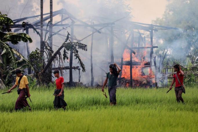 Men carry knives and slingshots as they walk past a burning house in Gawdu Tharya village near Maungdaw in Rakhine state in northern Myanmar on September 7, 2017. Photo: AFP