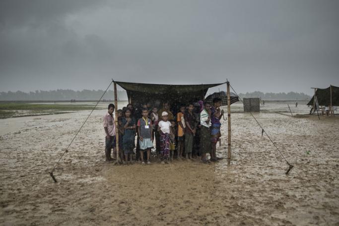 Rohingya Muslim refugees take shelter from the rain during a food distribution at Nayapara refugee camp in Bangladesh's Ukhia district on October 6, 2017. Photo: Fred Dufour/AFP
