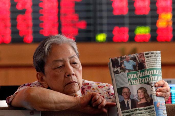 A Thai investor holds a newspaper reporting on US actor Tom Hanks' coronavirus case, as indicator boards show mainly red signs of falling share prices data at a stock brokerage in Bangkok, Thailand, 13 March 2020. Photo: EPA