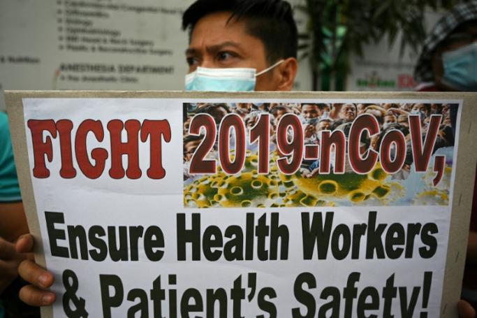 A health worker wearing a face mask holds a placard during a protest in front of a government hospital in Manila (AFP/File / Ted ALJIBE)