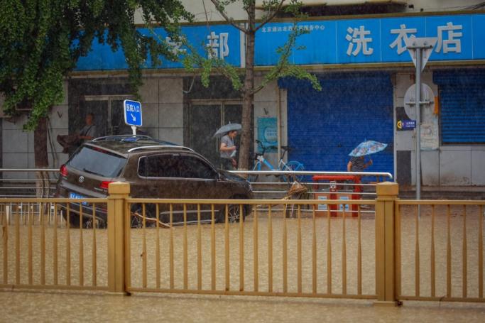 People walk next to a damaged by flood car during a downpour in Mentougou District, west of Beijing, China, 01 August 2023. Photo: EPA