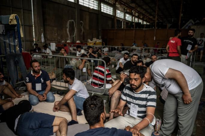 Survivors of a shipwreck sit inside a warehouse at the port in Kalamata town, on June 15, 2023, after a boat carrying migrants sank in international waters in the Ionian Sea. Photo: Angelos TZORTZINIS/AFP