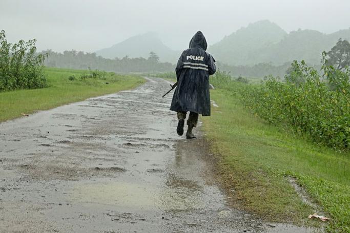 A Myanmar police officer in a rain coat patrols on a road in the ethnic Rakhine village of Chain Khar Li, an area close to fighting at Rathedaung township of northern Rakhine State, western Myanmar, 26 August 2017. Photo: Nyunt Win/EPA

