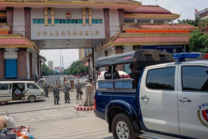 (File) Chinese border police guards keep watch as Myanmar migrant workers return from China amid the coronavirus pandemic at the Myanmar border gate in Muse in northern Shan state, May 12, 2020.