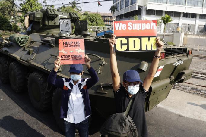 Demonstrators hold up placards supporting the 'civil disobedience movement' (CDM) in front of an armoured vehicle during a protest outside the Central Bank in Yangon, Myanmar, 15 February 2021. Photo: Lynn Bo Bo/EPA