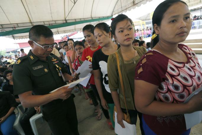 Thai military officer (L) checks the documents of Myanmar migrant workers queueing at the One Stop Service for the Registration of Migrant Workers in Samut Sakhon Provincial Social Security Office, in Samut Sakhon, southwest of the capital Bangkok, Thailand, 30 June 2014. Photo: Narong Sangnak/EP
