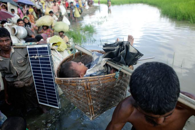 A Rohingya man carries his son in a basket while another carries a solar panel as newly arrived Rohingya refugees wade through the water canals between paddy field behind the border of Bangladesh after hundreds fled from Budichong, Myanmar, and were crossing the Naf river, near Palongkhali, Bangladesh, 09 October 2017. Photo: Abir Abdullah/EPA-EFE
