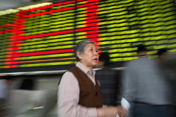 An elderly woman walks past a trading board at a securities exchange house in Shanghai, China. Photo: Qilai Shen/EPA
