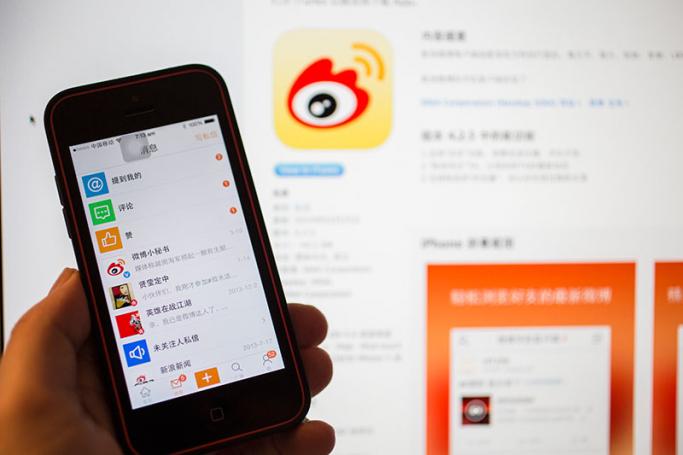 The Sina Weibo social networking app is seen against a background of the company logo on screen in Beijing, China. Photo: EPA
