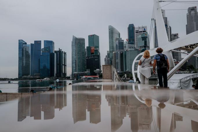 Reflected in a puddle, a couple is seen looking at the skyline of the financial district in Singapore. Photo: Wallace Woon/EPA