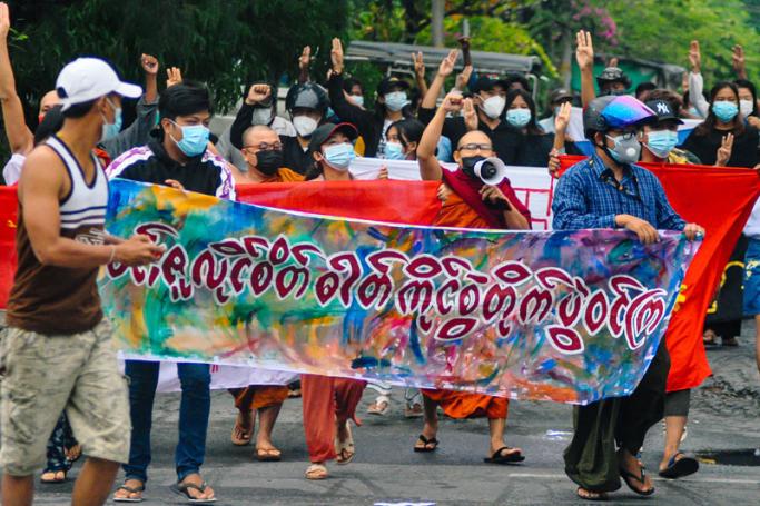 Buddhist monks walk with protesters as they hold a banner that reads, "Fight by keeping spirit of 7 July up" during a demonstration against the military coup in Mandalay on July 7, 2021.  Photo: AFP